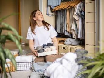 Ordnung im Kleiderschrank – Frau verstaut ihre Kleidung in Kisten und Körben.