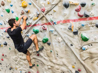 Bouldering jak zacząć – młody boulderowiec rozwiązuje problem na ściance wspinaczkowej.