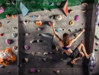 Boulder para principiantes: una chica practica boulder en la pared de una sala de escalada para fortalecer sus músculos.