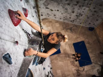 Una mujer hace escalada top-rope en la pared de un gimnasio de escalada.