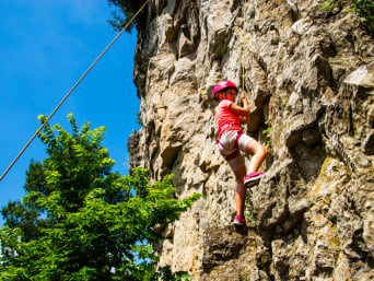Una niña practica escalada en pared de roca natural.