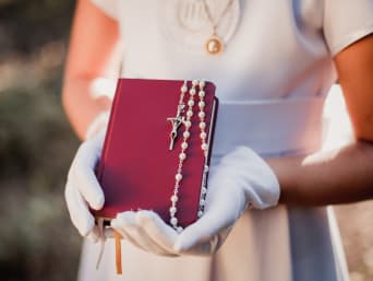 Regalos de primera comunión: una niña vestida de blanco con un rosario y una biblia en las manos.