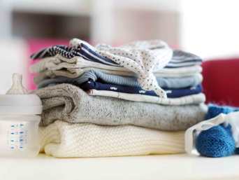 Baby-Erstausstattung – Ein Stapel Kleidung und ein Fläschchen. 