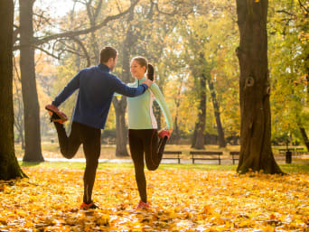 Bieganie jesienią: dwójka biegaczy wykonuje ćwiczenia rozciągające w parku.