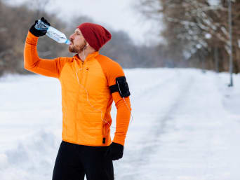 Courir en hiver : un joggeur fait une pause et bois de l’eau.