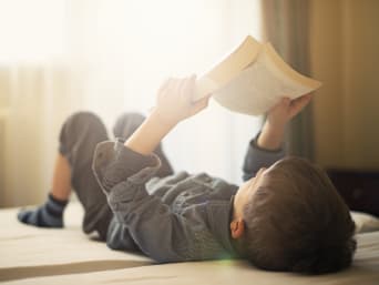 Jongen ligt op bed en leest een boek.