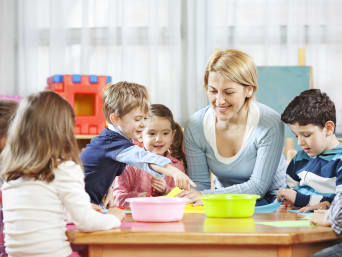 Lesespiele: Kinder sitzen mit einer Betreuerin am Tisch und lernen spielend Lesen.