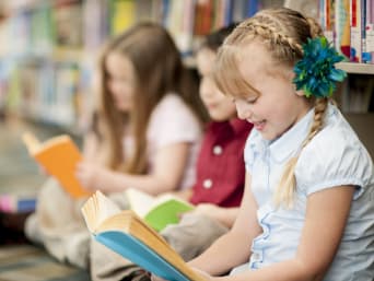 Lesen lernen: Mädchen liest mit Freunden in der Bibliothek.