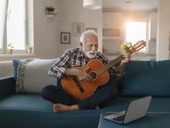 Activiteiten voor ouderen – Oudere man leert gitaarspelen met behulp van een onlinefilmpje.