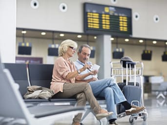 Een echtpaar zit op het vliegveld en kijkt samen naar een smartphone.