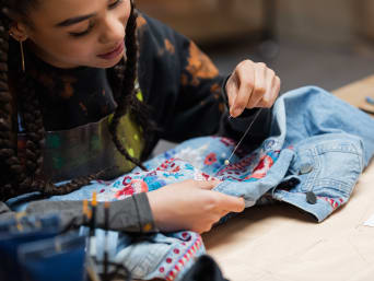 Jeansjacke besticken – Frau bestickt eine Jeansjacke mit Perlen. 