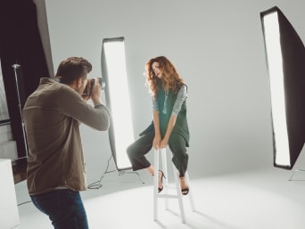 Training as a fashion photographer: a young photographer doing a photo shoot with a female model at a photo studio.