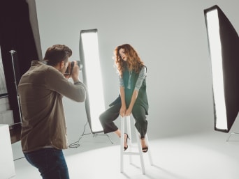 A fashion photographer doing a photoshoot with a model in a photo studio.