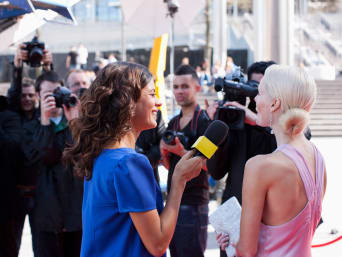 Una periodista de moda entrevista en la alfombra roja a una mujer vestida elegantemente.