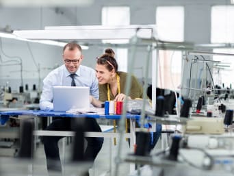 Bekleidungstechnik: Zwei Personen arbeiten in einer Textilfabrik an einem Laptop.