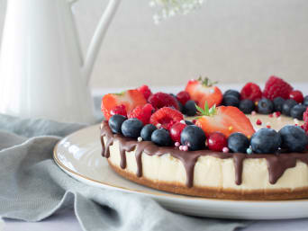 Finished cheesecake with fruit and chocolate icing on the table.