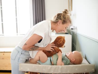 Baby anziehen – Mutter macht das Anziehen mit einem Teddy zum Spiel.