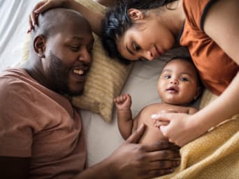 Pierwsze dni z niemowlakiem: mama i tata leżą z dzieckiem w łóżku.