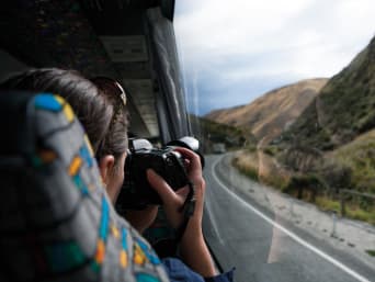 Nachhaltig reisen: Frau verreist im Reisebus und macht Fotos von vorbeiziehenden Landschaften.