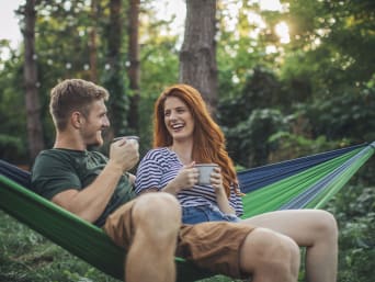 Plastic-free travel: holidaymakers relaxing in a hammock and drinking out of enamel mugs.