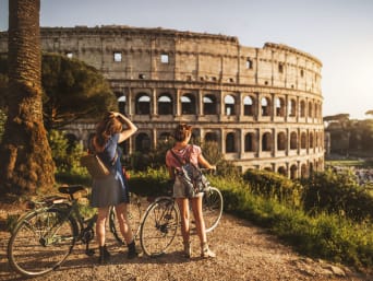 Nachhaltiger Urlaub: Zwei Radfahrerinnen betrachten das Kolosseum in Rom.