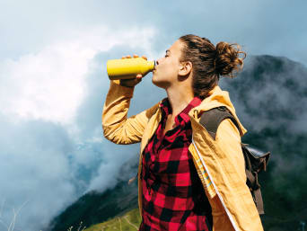 Sustainable holidays: a woman drinking out of a stainless steel water bottle.