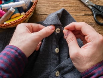 Repairing old clothes: a man is sewing a button back onto his shirt.
