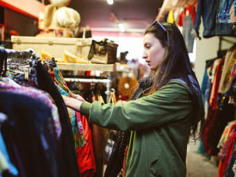 Vrouw doorzoekt kledingrekken in kringloopwinkel.