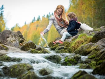 Mutter und Tochter sitzen an einem Bach im Wald und hören dem rauschenden Wasser zu.