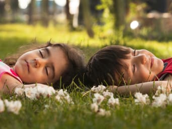 Deux enfants allongés dans une prairie, les yeux fermés, écoutant les sons de la nature.