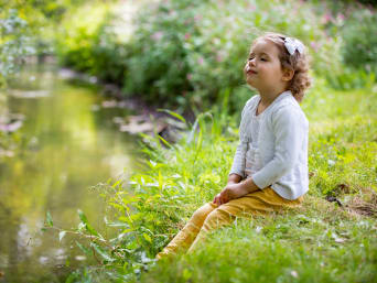 Petite fille assise au bord d'une rivière, les yeux fermés, écoutant le clapotis de l'eau.