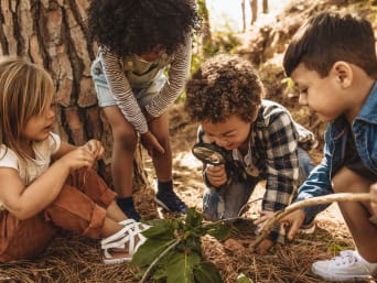 Spiele im Wald – Kinder untersuchen den Waldboden mit einer Lupe.