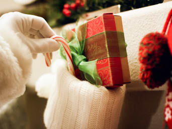 Mikołaj obdarowuje podarkami wypełniając nimi skarpetę na prezenty.