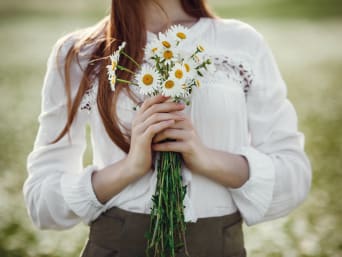 Oktoberfest outfit zonder Dirndl: jonge vrouw in witte blouse houdt een boeket bloemen in haar handen.
