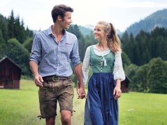 C&A Lederhosen Style-Guide: Junges Paar in Tracht läuft über eine Wiese.