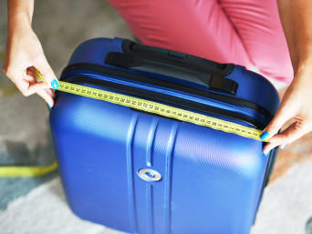 Handgepäck Masse: Eine Frau misst ihren Koffer mit einem Massband.