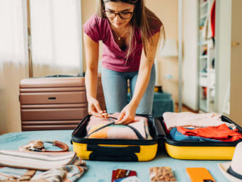 Správné balení na dovolenou: Žena si balí oblečení na cestu do cestovního kufru.