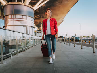 Women’s travel outfits: a young woman wearing a casual outfit wheeling her suitcase behind her at an airport.