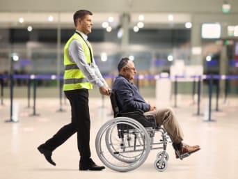 Viaggi per disabili in carrozzina: uomo anziano su sedia a rotelle viene assistito all’aeroporto.