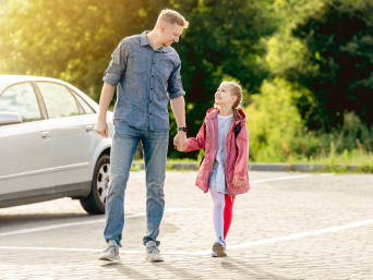 Kinder mit dem Auto zur Schule bringen – Vater parkt in einer Nebenstraße und läuft mit seiner Tochter zur Schule.