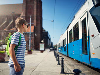 Dojazd do szkoły transportem publicznym: dziecko czeka na przystanku na przyjazd tramwaju.