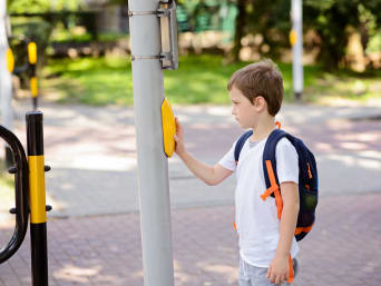 Zu Fuß zur Schule gehen: Kleiner Junge wartet an einer Ampel.