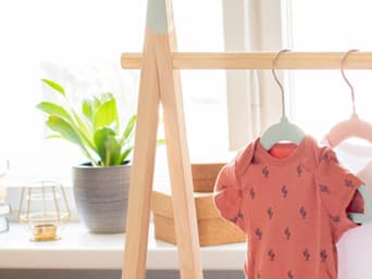 Baby-Erstausstattung Checkliste: Erstlingsbekleidung auf einem Kleiderständer.