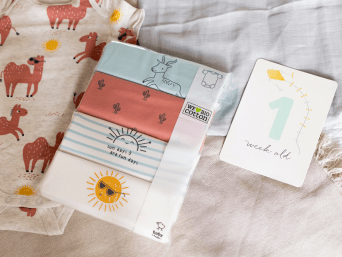Baby-Erstausstattung Checkliste: Ein Multipack Erstlingsbekleidung auf einer Decke ausgebreitet.