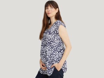 What to wear during pregnancy: a woman in the first trimester covering up her baby bump with a loose-fitting top.