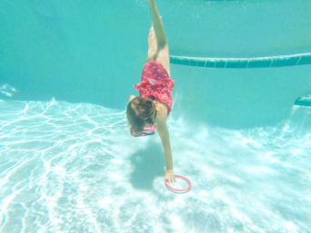 Specjalna karta pływacka: dziewczynka nurkuje w basenie po obciążeniowe kółko podczas egzaminu na kartę pływacką.