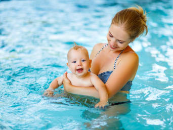Clases de natación para bebés: una madre sostiene a su bebé en una piscina.