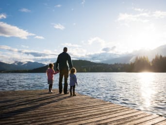 Two little girls with dad on the jetty looking at the mountain lake.