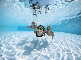Regole in piscina: tre bambini nuotano sul fondo della piscina indossando gli occhialini.