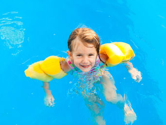 Dziewczynka w rękawkach do pływania uczy się utrzymywać na wodzie w brodziku